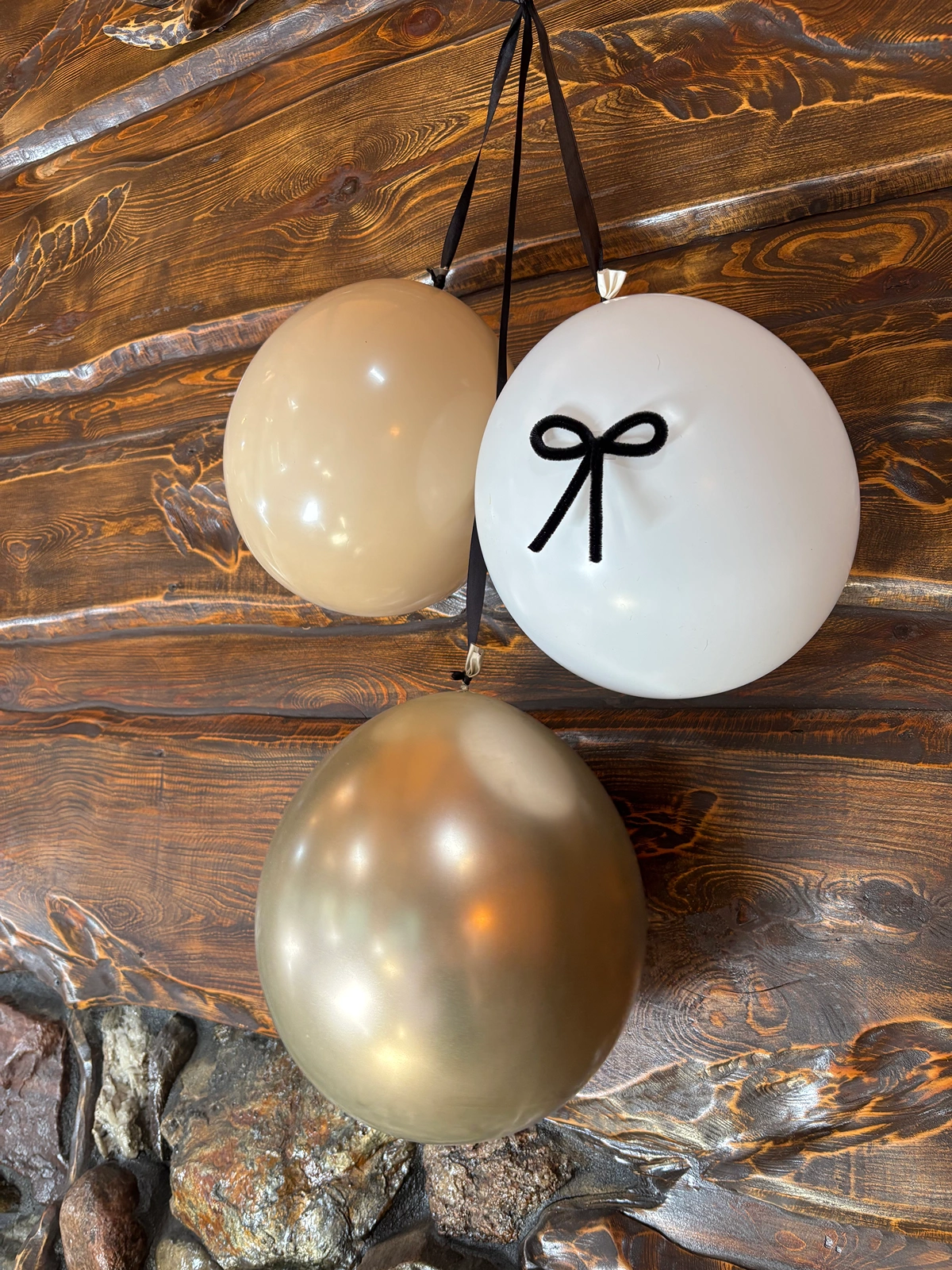 Zbliżenie na zestaw balonów: chromowane złoto, beż i biel z czarną kokardą